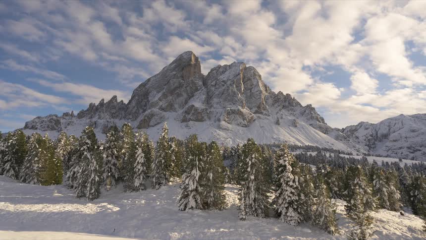 Time-lapse of clouds moving across a blue sky over a majestic snow-covered mountain and a forest of pine trees