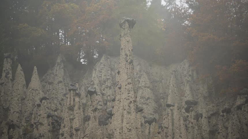 A static shot of the unique earth pyramid rock formations in a forest on a foggy autumn day