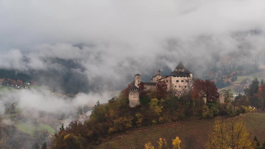 Ethereal timelapse shows clouds and fog swirling around a historic castle nestled in an autumn valley