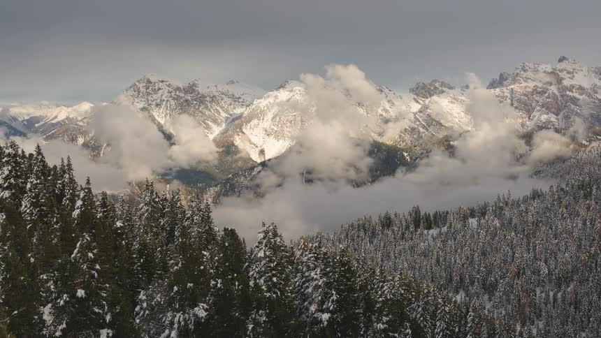 A majestic timelapse of clouds drifting through a snowy mountain valley above a vast, snow-covered pine forest