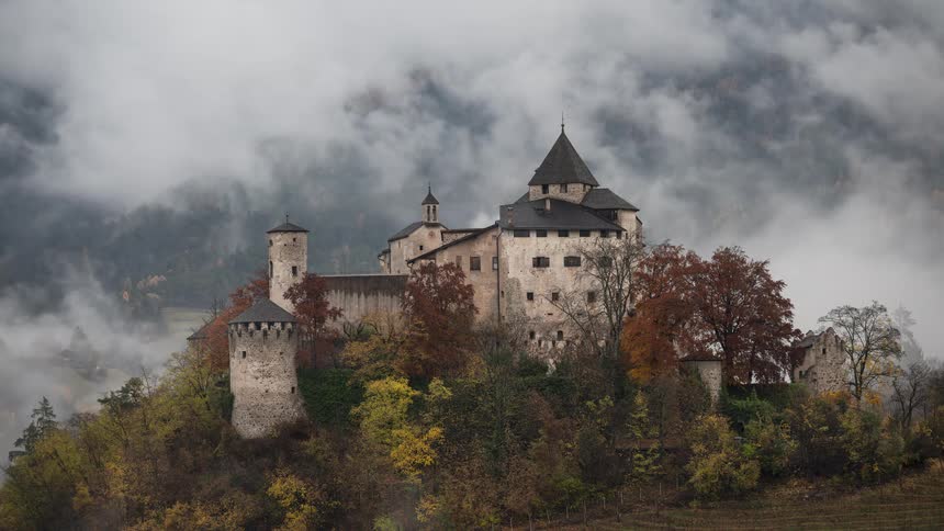 A time-lapse of a historic medieval castle on a hill as thick fog and clouds roll through the valley during autumn
