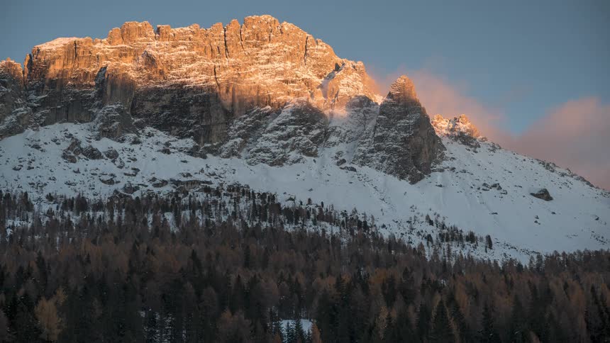 A stunning timelapse captures the golden sunset fading over a majestic, snow-covered mountain peak and the colorful autumn forest below