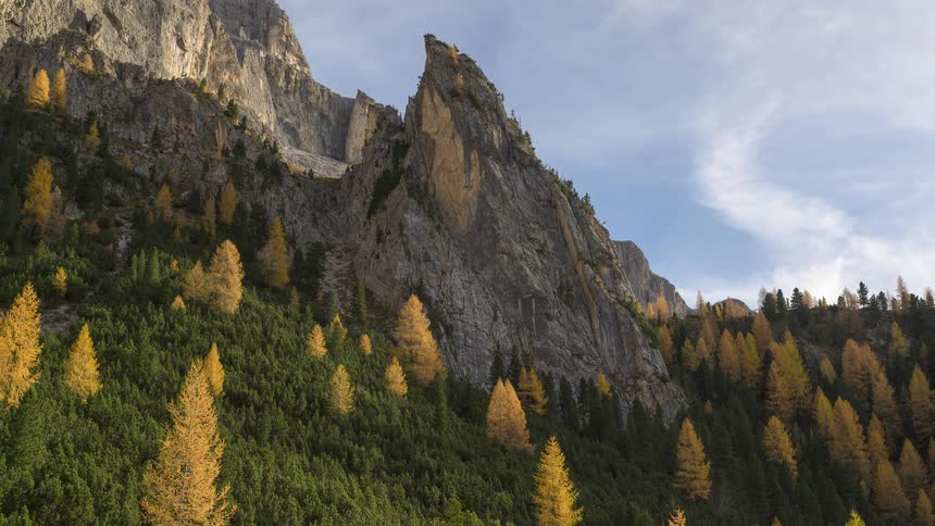 A stunning timelapse of clouds moving over a majestic mountain peak covered with a forest of green and golden yellow autumn trees