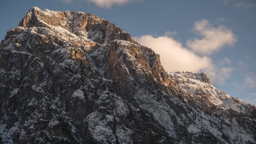 A majestic snow-dusted mountain peak stands tall as clouds drift by in a beautiful timelapse