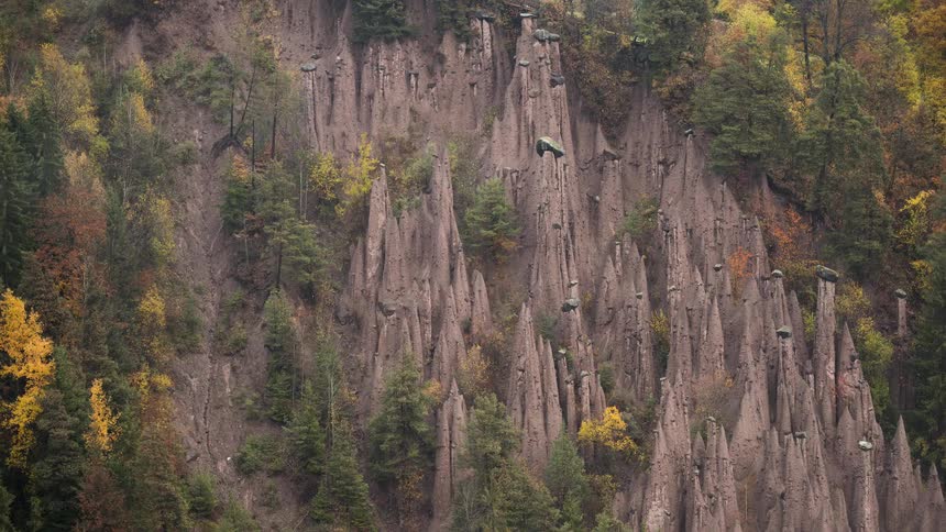 A time-lapse of mystical fog clearing to reveal the unique earth pyramids of Ritten, nestled in an Italian alpine forest during autumn