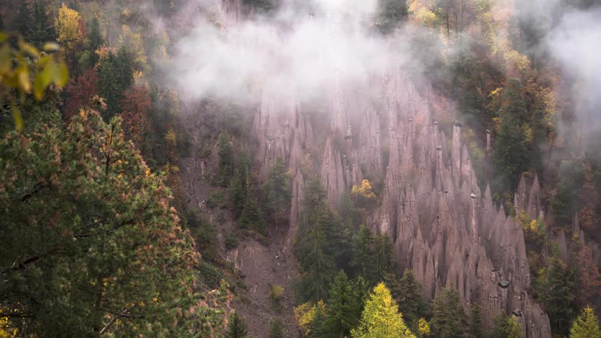 Time-lapse of ethereal fog rolling through an autumn forest, obscuring unique geological earth pyramid formations
