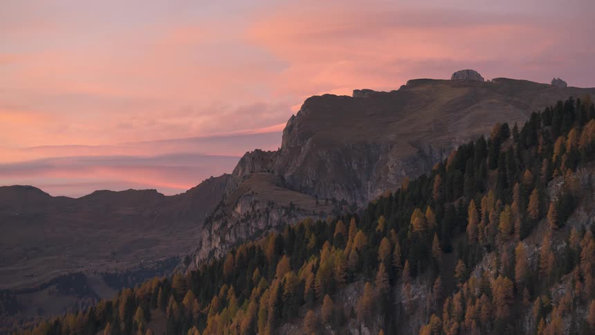 A breathtaking timelapse of a vibrant pink and orange sunset illuminating a majestic mountain range covered in autumn forests