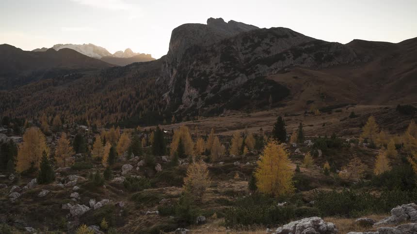 A stunning time-lapse captures the sun setting behind majestic mountain peaks, casting a golden glow over a valley of vibrant yellow autumn trees