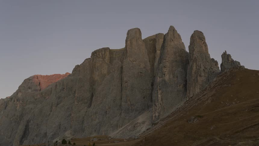 A breathtaking time-lapse captures the transition from a golden hour sunset to a beautiful purple twilight over the rugged Sella Towers in the Dolomites