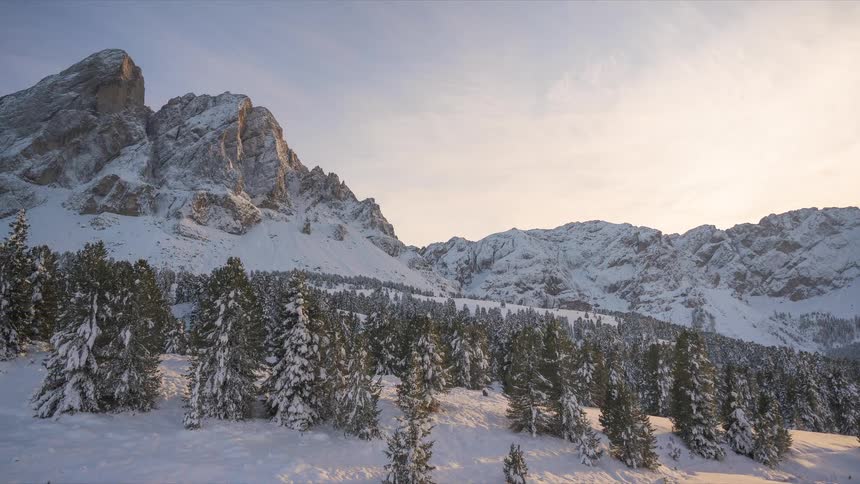 Stunning panoramic view of a snow-covered mountain landscape with a pine forest at golden hour