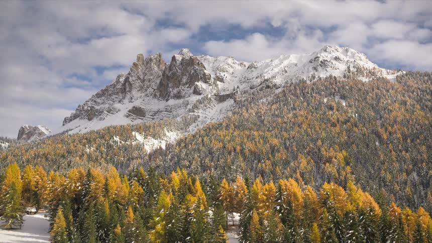 A scenic timelapse captures clouds and sunlight moving across a snow-capped mountain range above a vibrant autumn forest