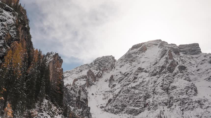 A time-lapse of wispy clouds moving swiftly over majestic snow-covered mountains on a bright, sunny day