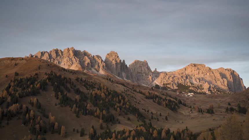 A day-to-night timelapse shows a beautiful sunset and alpenglow over the rugged Dolomite mountains in autumn, transitioning to a starry night sky