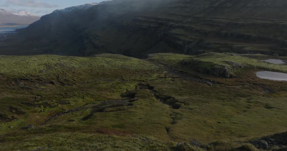 A drone flies over a young child in a colorful outfit standing on a hilltop, revealing the vast, mossy green landscape of Iceland