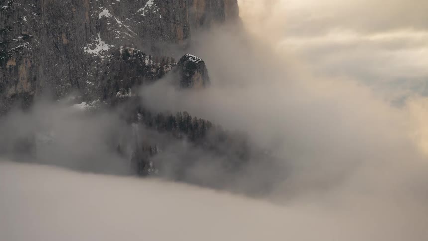 A majestic, snow-capped mountain peak emerges from a thick sea of rolling clouds in a stunning timelapse