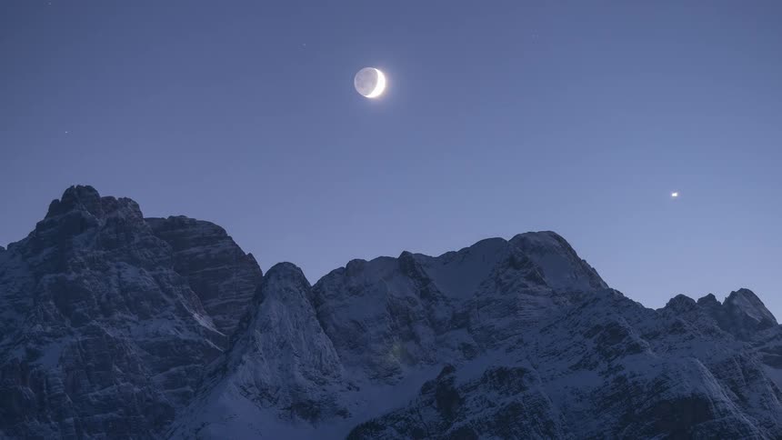 A stunning timelapse shows the moon changing phases from a crescent to full as it moves across the starry night sky above a snowy mountain range