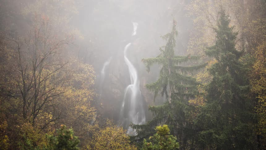 A timelapse of a waterfall in an autumn forest as morning mist slowly dissipates, revealing the rocky cascade