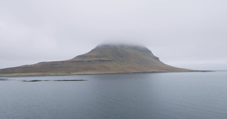 A static shot of the iconic Kirkjufell mountain in Iceland, its peak enveloped in thick clouds on a moody, overcast day