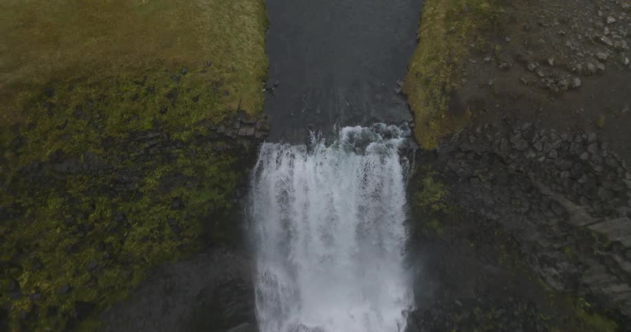 A high-angle aerial view slowly pulls back to reveal a stunning waterfall cascading over a mossy cliffside