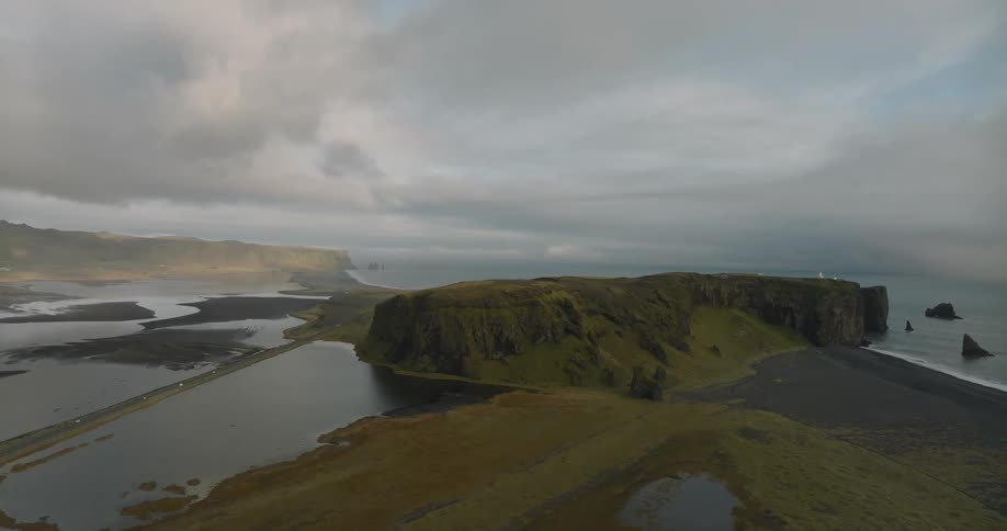 A static wide aerial view showcases the dramatic, moody landscape of the Dyrhólaey peninsula in Iceland on an overcast day