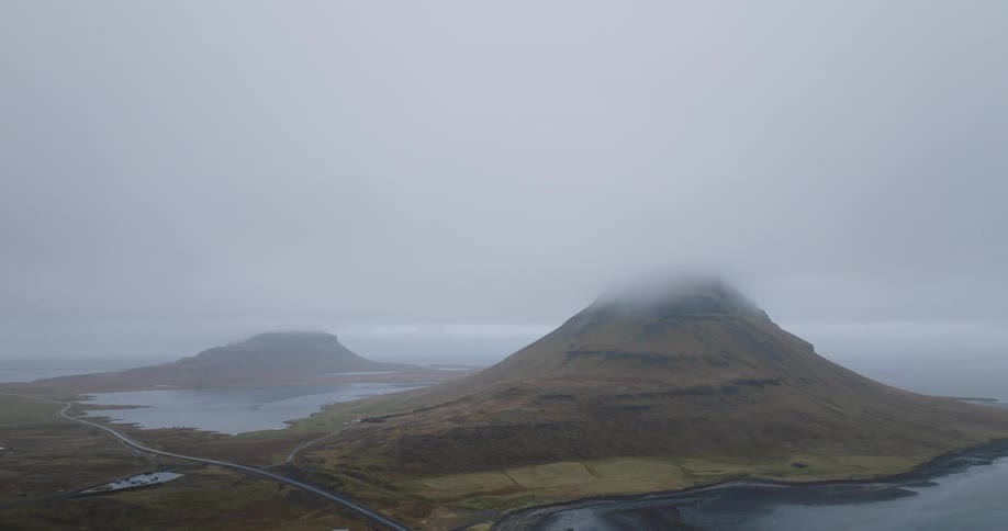 A cinemagraph of a moody Icelandic landscape featuring a large mountain with its peak shrouded in slow-moving clouds and fog