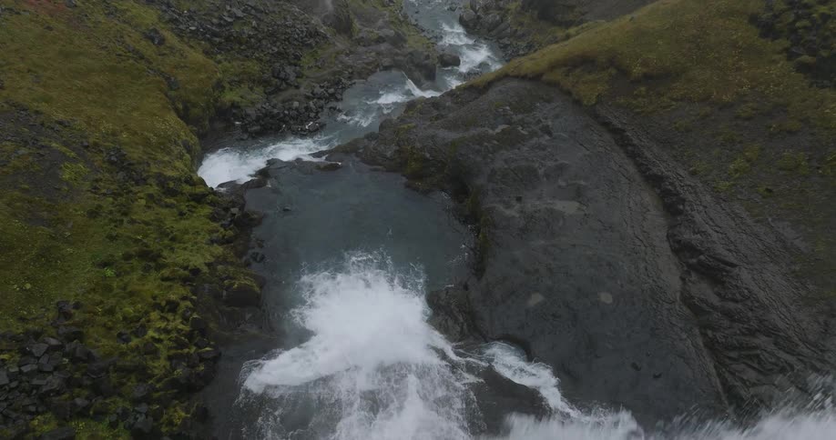 A dramatic first-person aerial view follows a river over the edge of a cascading waterfall into a rocky canyon below