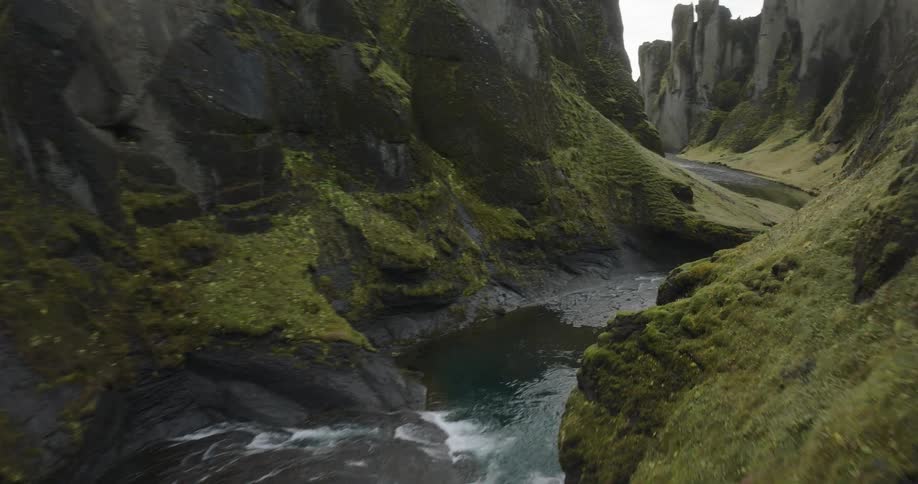 An immersive aerial journey through a deep, green canyon carved by a winding river in Iceland