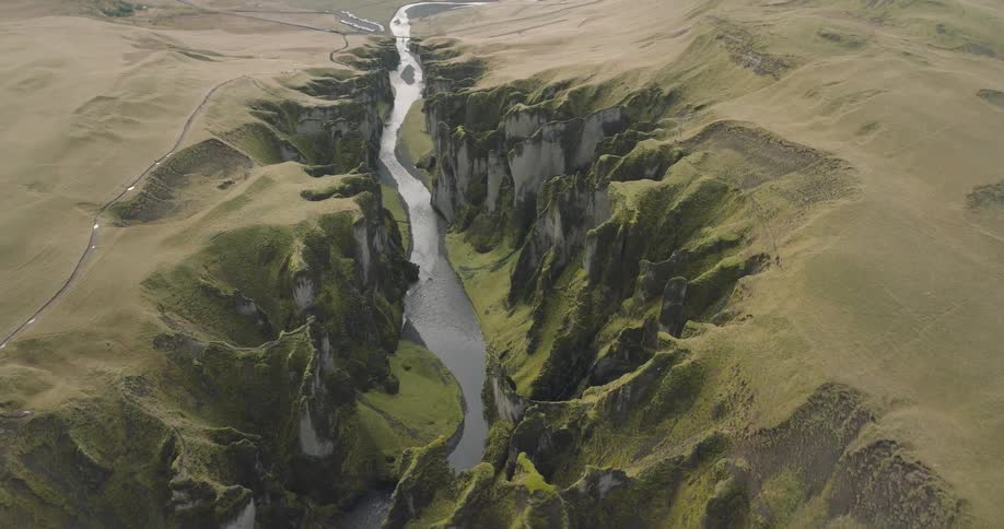 An epic aerial view pulls back to reveal the breathtaking scale of a deep river canyon winding through Iceland's vast, green highlands