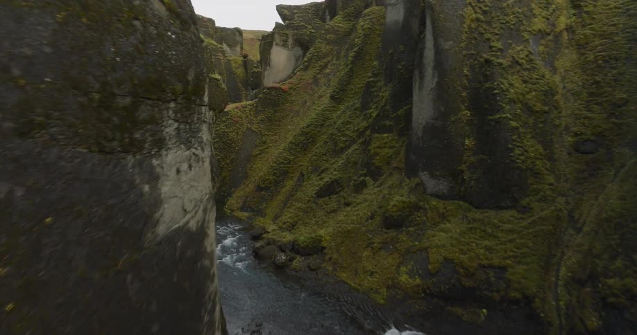 An immersive aerial journey flies through the majestic Fjaðrárgljúfur canyon in Iceland, revealing its deep, moss-covered walls and the winding river below