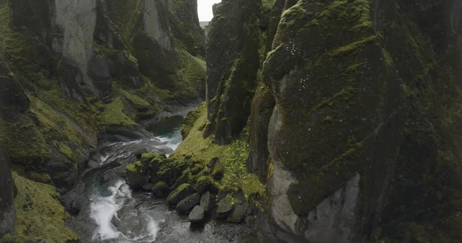 An epic aerial view flying over the Fjadrargljufur canyon in Iceland as it winds through the green, mossy valley