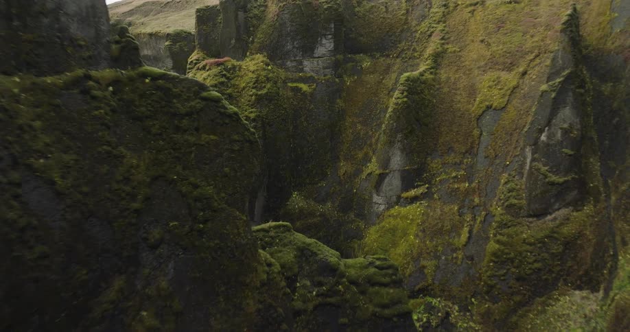 A slow aerial descent into a dramatic, moss-covered canyon reveals a winding river below