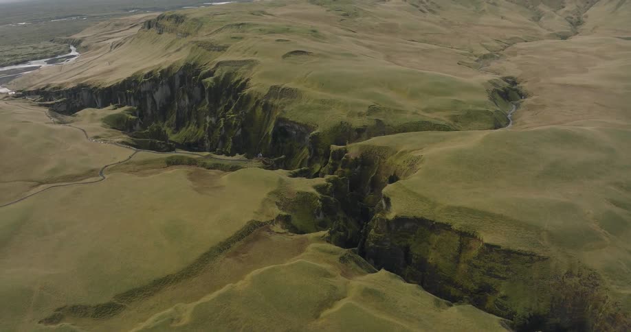 A slow, sweeping aerial shot reveals the immense scale of a dramatic green canyon cutting through the vast Icelandic highlands