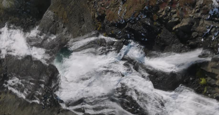 A powerful waterfall cascades down a rugged, rocky cliff in a stunning aerial view that slowly rises to reveal the landscape