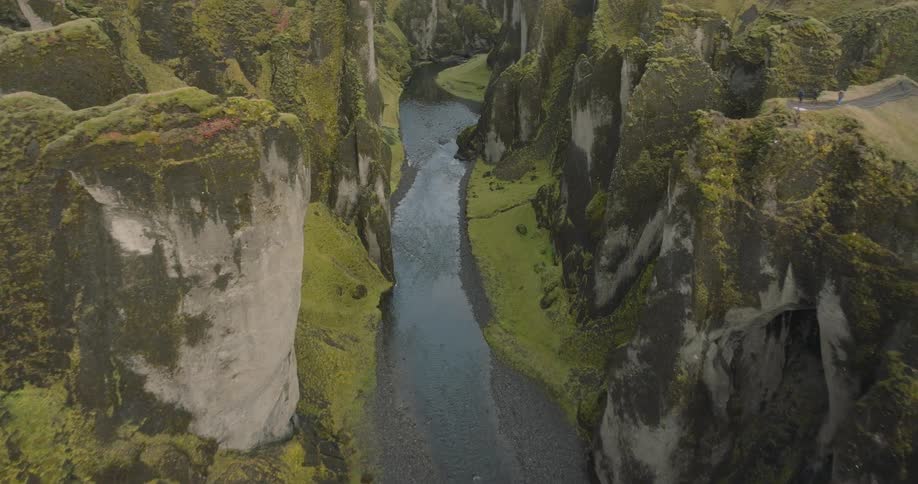 An epic aerial view flying through a majestic moss-covered canyon with a river flowing through it in the Icelandic highlands