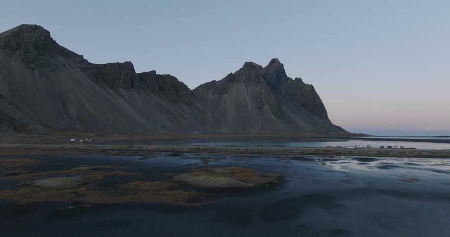 A serene aerial view of Iceland's iconic Vestrahorn mountain range over a tranquil black sand lagoon at twilight