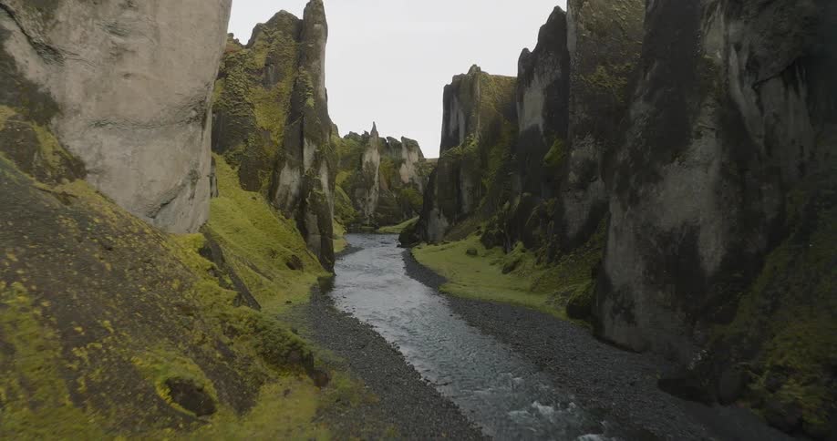 An immersive aerial shot flies slowly down a majestic green canyon as a river flows through the valley floor