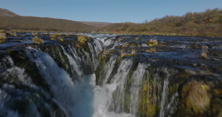 A breathtaking aerial journey upstream along the vibrant blue waters of the Bruarfoss waterfall in Iceland