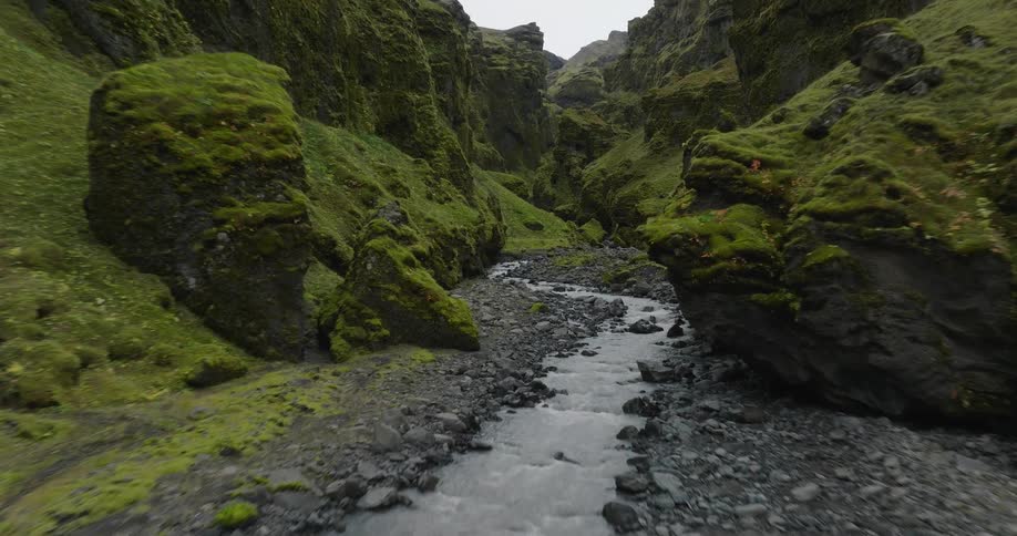 A breathtaking aerial view follows a rocky river winding through a dramatic and lush green canyon in Iceland