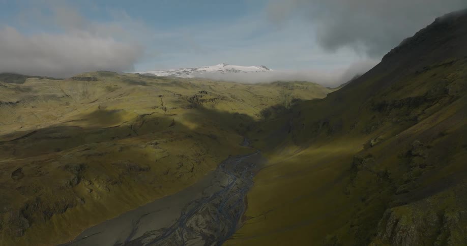 A beautiful timelapse captures sunlight and shadows sweeping across a vast green valley and river, with a snow-capped glacier visible in the distance