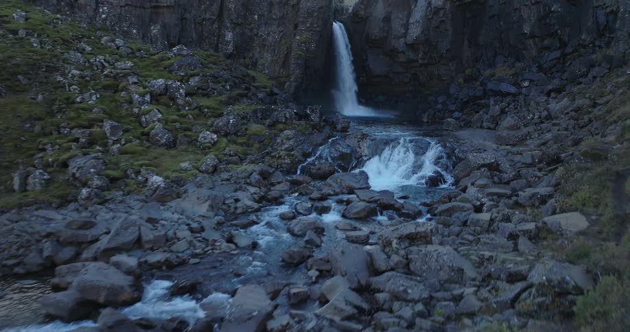 A dramatic aerial shot pulls back to reveal a beautiful waterfall cascading down a rocky cliff face into a winding river below