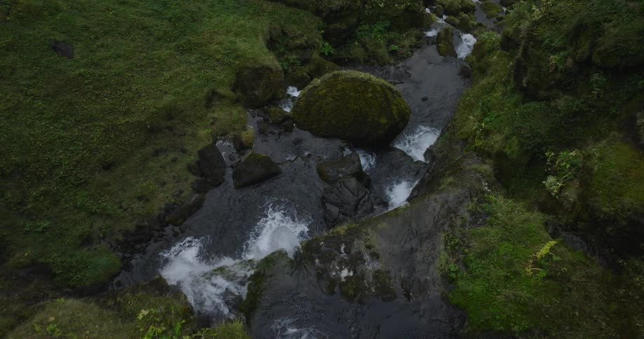 An overhead aerial shot slowly pushes into a beautiful, mossy Icelandic river cascading down a rocky canyon