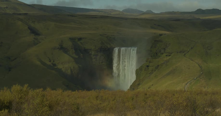 Expansive wide shot of the Skógafoss waterfall in Iceland as it plunges into a gorge, creating a misty rainbow