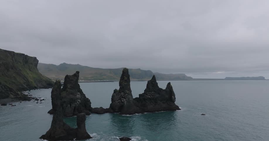 An aerial view slowly circles the majestic Reynisdrangar sea stacks rising from the North Atlantic Ocean off the coast of Iceland