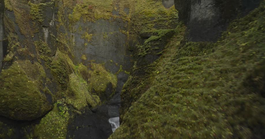 An immersive aerial flight soars through a deep, moss-covered river canyon in the epic Icelandic highlands