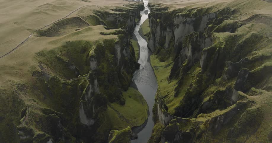 An awe-inspiring aerial pullback shot reveals the majestic Fjaðrárgljúfur canyon in Iceland, with its steep, moss-covered walls and a winding river below