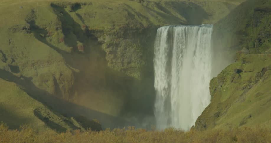 The majestic Skógafoss waterfall in Iceland powerfully cascades down a green cliffside, creating a misty spray and a faint rainbow