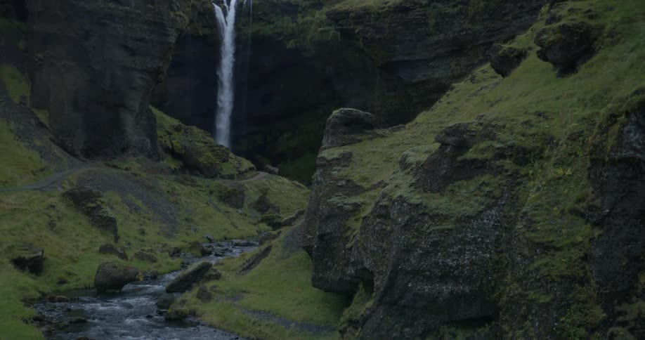 A steady river flows through a mossy green canyon revealing the hidden Kvernufoss waterfall in Iceland