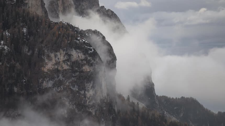 Clouds slowly move around a majestic mountain cliff with a light dusting of snow