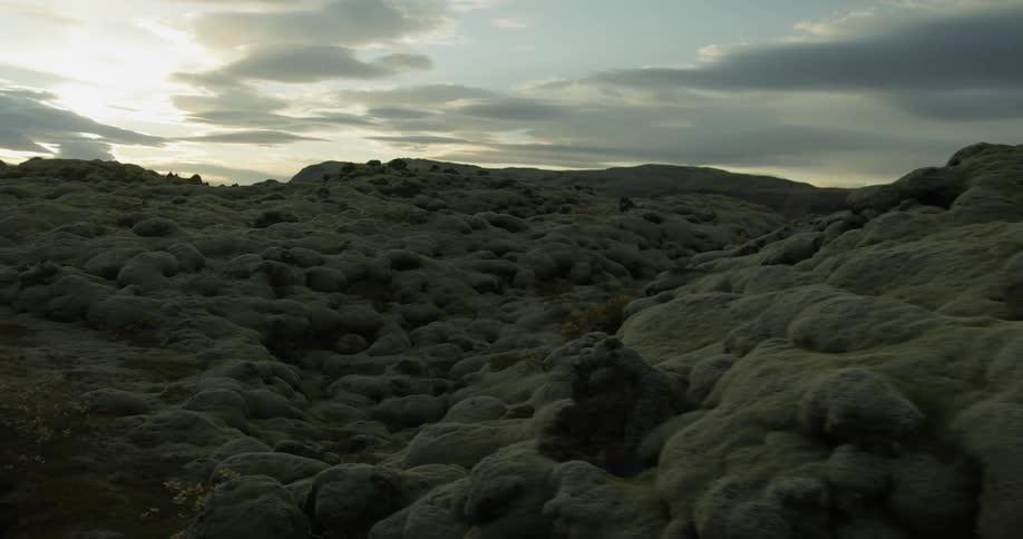 A slow, mysterious glide over an ancient, moss-covered volcanic lava field at dusk