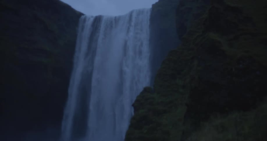 A dramatic slow pan reveals the powerful Skógafoss waterfall cascading down a mossy cliff in Iceland at dusk
